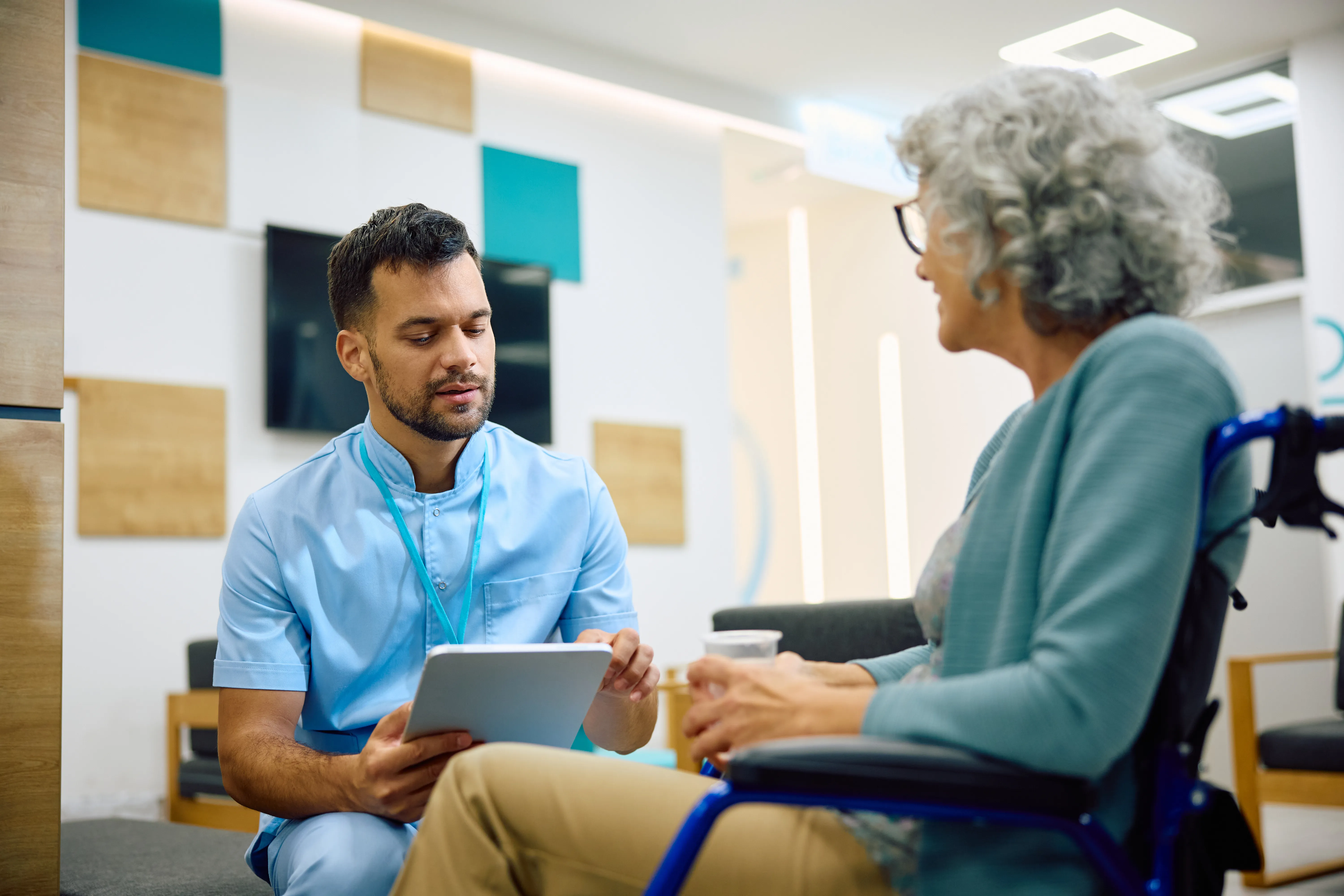 A medical assistant talking with an older patient using a wheelchair